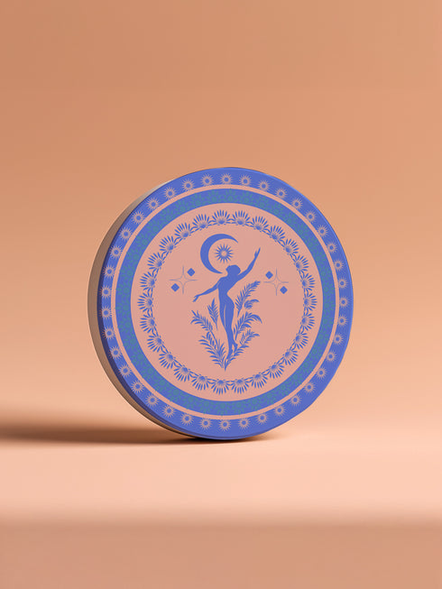 Round ceramic coaster featuring a silhouetted dancing figure reaching toward a crescent moon, surrounded by concentric rings of stars and floral patterns in blue on peach background